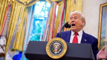 Donald Trump speaks animatedly at the presidential podium in the Oval Office, appearing mid-sentence during a fiery address