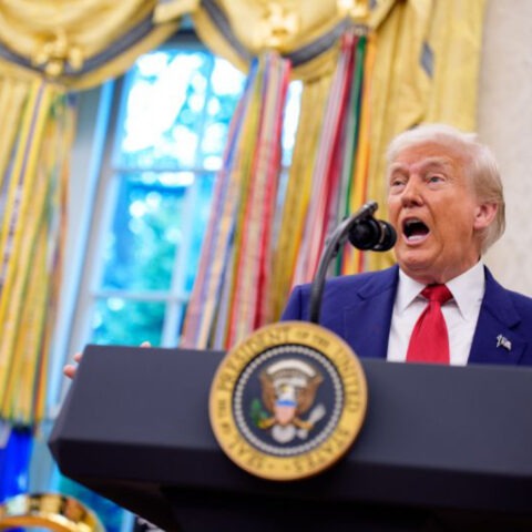 Donald Trump speaks animatedly at the presidential podium in the Oval Office, appearing mid-sentence during a fiery address