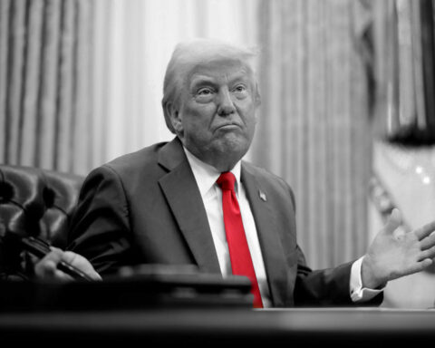 Donald Trump at the Resolute Desk with a confused expression, in black and white except for his red tie