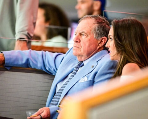 Bill Belichick and Jordon Hudson seated together, speaking privately