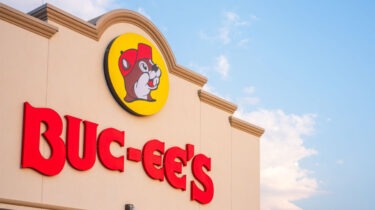 Buc-ee’s store sign with beaver logo on building exterior against a blue sky.