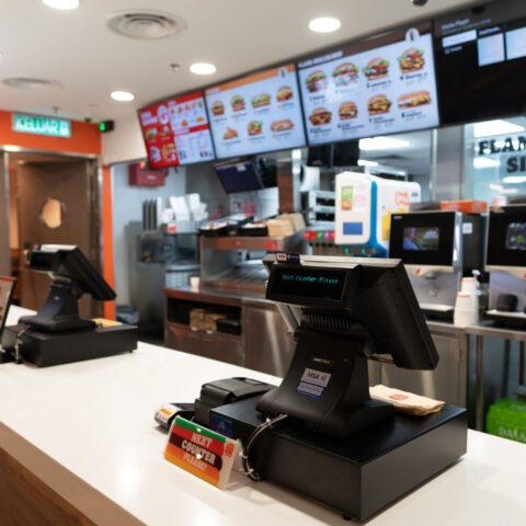 Empty fast food restaurant counter with touchscreen registers and digital menus visible