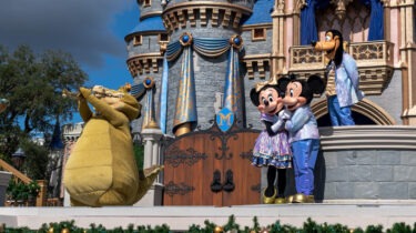 Disney characters Mickey Mouse, Minnie Mouse, Goofy, and Louis the alligator perform on stage in front of Cinderella Castle at Walt Disney World.