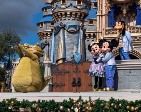Disney characters Mickey Mouse, Minnie Mouse, Goofy, and Louis the alligator perform on stage in front of Cinderella Castle at Walt Disney World.