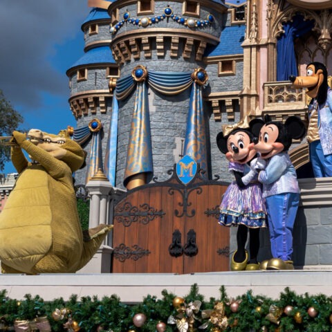 Disney characters Mickey Mouse, Minnie Mouse, Goofy, and Louis the alligator perform on stage in front of Cinderella Castle at Walt Disney World.