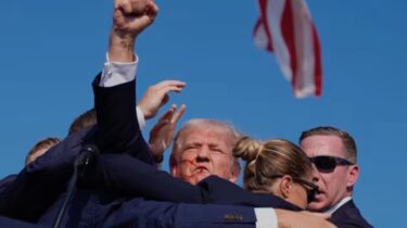 Donald Trump being escorted away after assassination attempt, blood on face