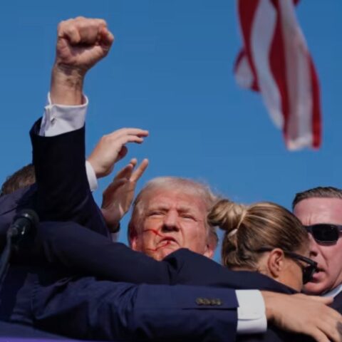Donald Trump being escorted away after assassination attempt, blood on face