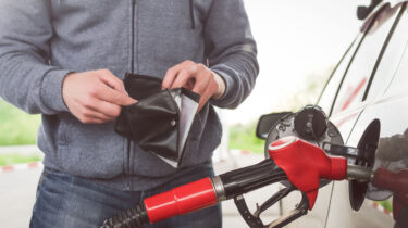 Man looks inside empty wallet while fueling car