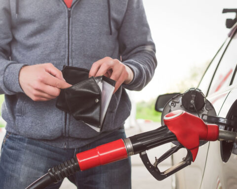 Man looks inside empty wallet while fueling car