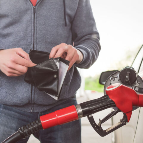 Man looks inside empty wallet while fueling car