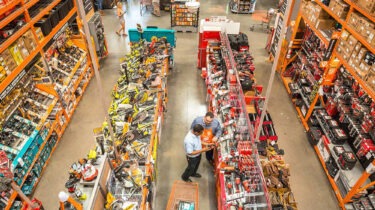 Men staring blankly at power tools inside a brightly lit Home Depot