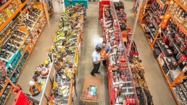 Men staring blankly at power tools inside a brightly lit Home Depot