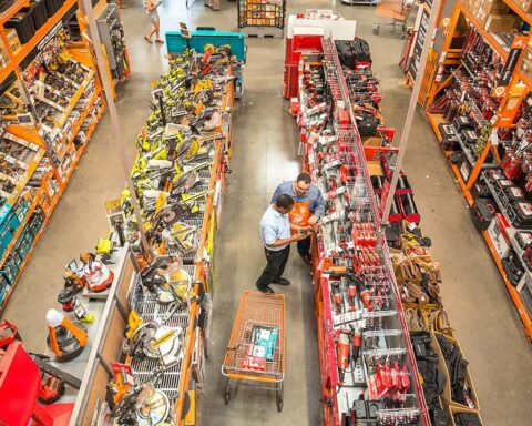 Men staring blankly at power tools inside a brightly lit Home Depot