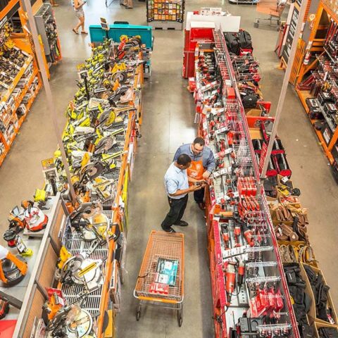 Men staring blankly at power tools inside a brightly lit Home Depot