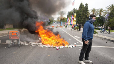 Protester stands near burning debris and smoke during street demonstration in Los Angeles