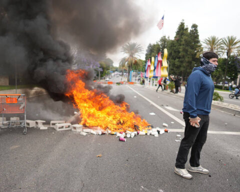 Protester stands near burning debris and smoke during street demonstration in Los Angeles