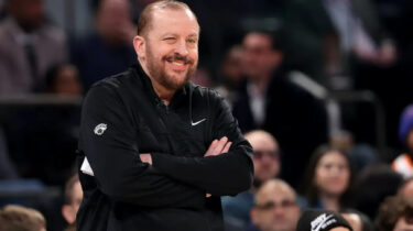 New York Knicks coach Tom Thibodeau winks while smiling courtside during an NBA game.