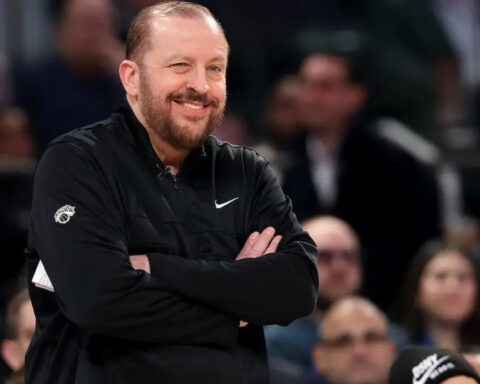 New York Knicks coach Tom Thibodeau winks while smiling courtside during an NBA game.