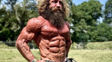 Liver King shirtless and flexing with primal intensity in a sunny field