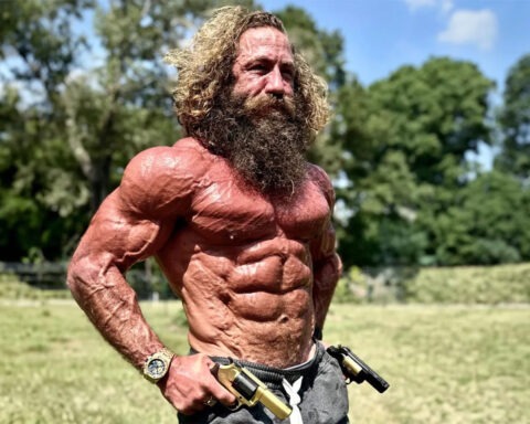 Liver King shirtless and flexing with primal intensity in a sunny field