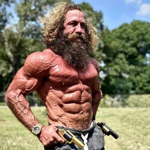 Liver King shirtless and flexing with primal intensity in a sunny field