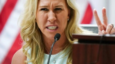 Marjorie Taylor Greene speaking intensely at a congressional hearing, gesturing with fingers raised