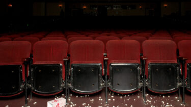 Empty theater seats with scattered popcorn and a tipped popcorn box on the floor, symbolizing a popcorn shortage.