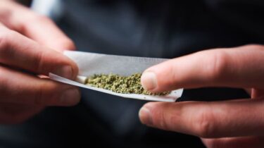 Close-up of a confused man holding a joint while reading health warning
