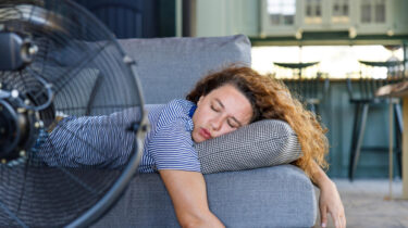 Woman passed out on couch in front of large fan during heatwave