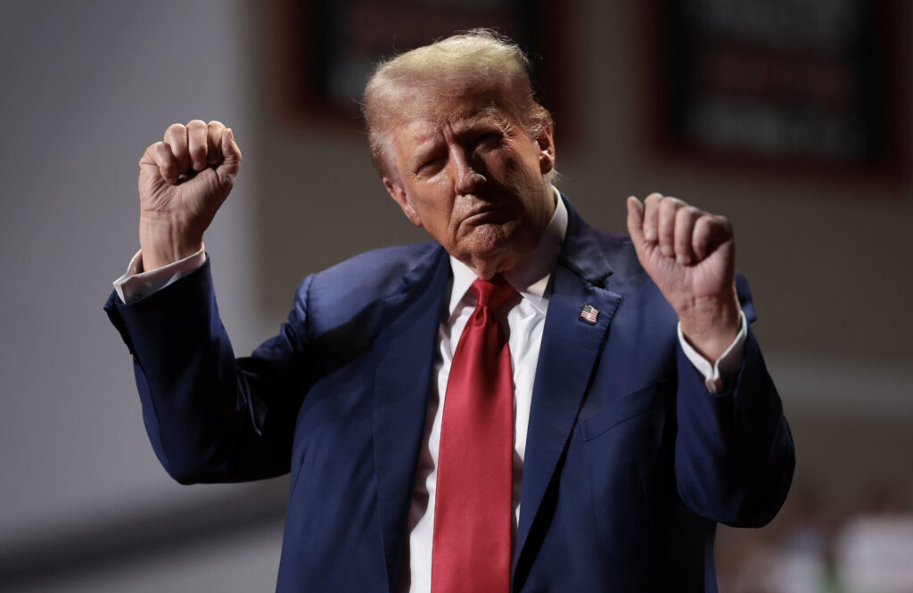 Donald Trump raises fists on stage in dark suit and red tie