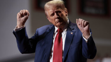 Donald Trump raises fists on stage in dark suit and red tie