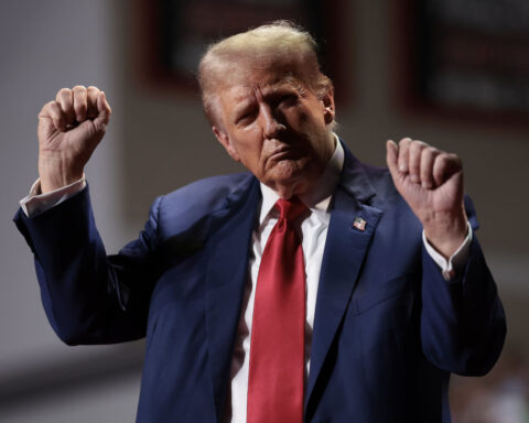 Donald Trump raises fists on stage in dark suit and red tie