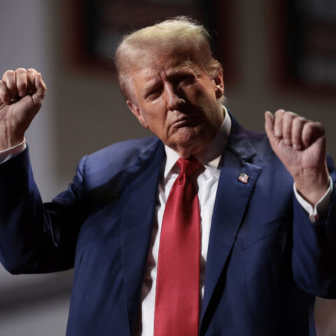 Donald Trump raises fists on stage in dark suit and red tie