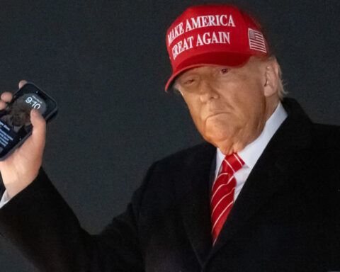 Donald Trump holding smartphone with MAGA hat while exiting Air Force One
