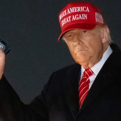Donald Trump holding smartphone with MAGA hat while exiting Air Force One