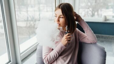 Woman vaping near window with large cloud of vapor