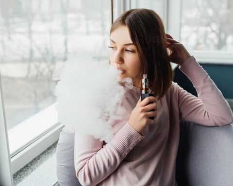 Woman vaping near window with large cloud of vapor