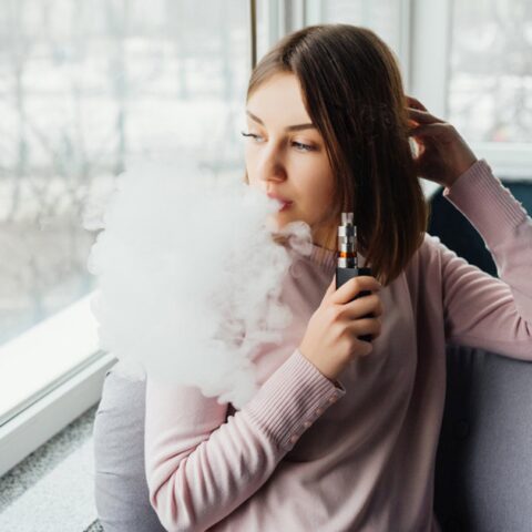 Woman vaping near window with large cloud of vapor