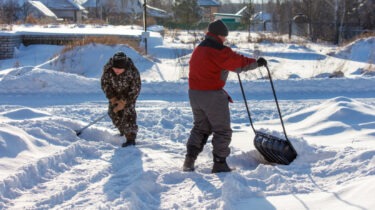 Two men are shoveling snow with a large black plastic bag