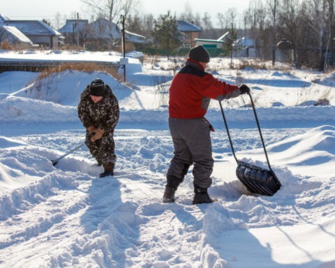 Two men are shoveling snow with a large black plastic bag