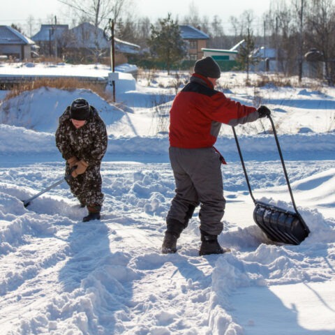 Two men are shoveling snow with a large black plastic bag