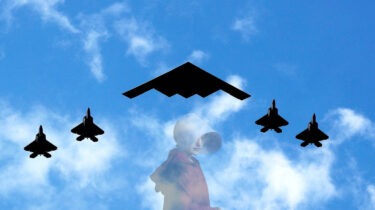 A B2 stealth bomber flies overhead accompanied by fighter jets.