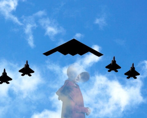 A B2 stealth bomber flies overhead accompanied by fighter jets.