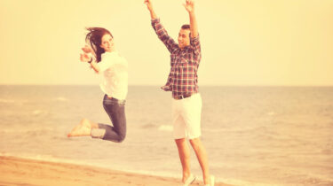 Happy couple jumping with joy on a beach, smiling and carefree under a warm golden sky