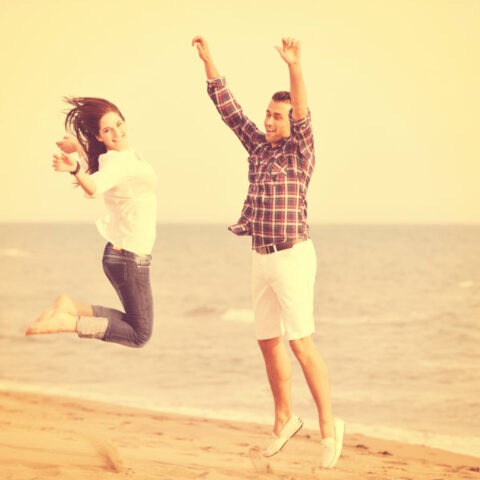 Happy couple jumping with joy on a beach, smiling and carefree under a warm golden sky