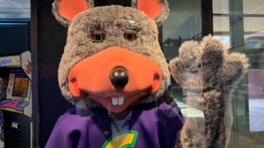 Chuck E. Cheese mascot being arrested by police officer inside restaurant