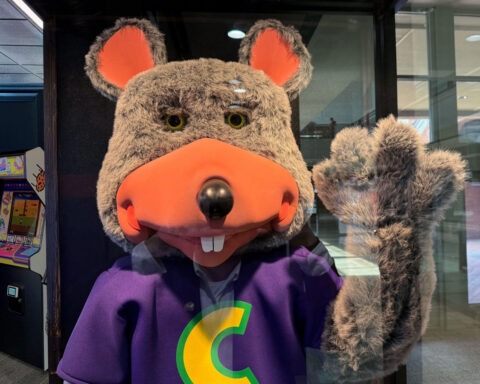 Chuck E. Cheese mascot being arrested by police officer inside restaurant