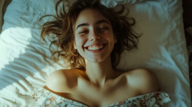 Smiling young woman lying on bed enjoying morning light and comfort