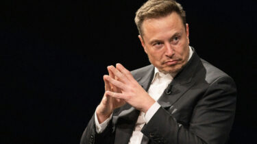 Elon Musk sitting with fingers steepled, plotting something strange