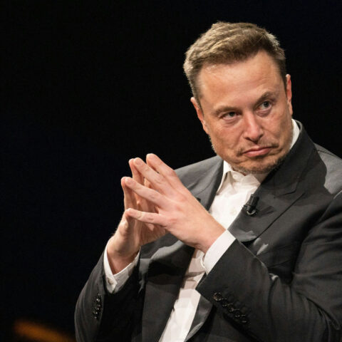 Elon Musk sitting with fingers steepled, plotting something strange